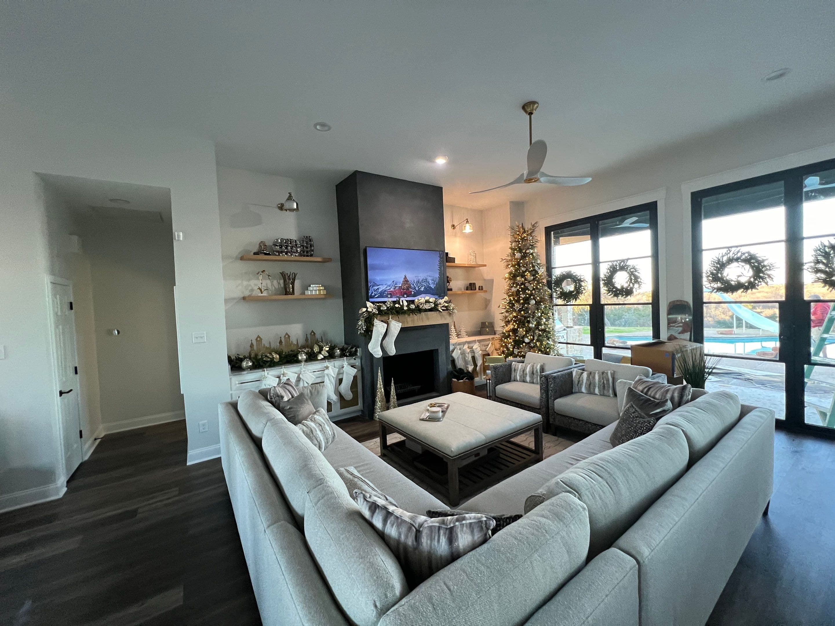 Modern living room with a gray sectional, lit Christmas tree, and festive fireplace decorations.