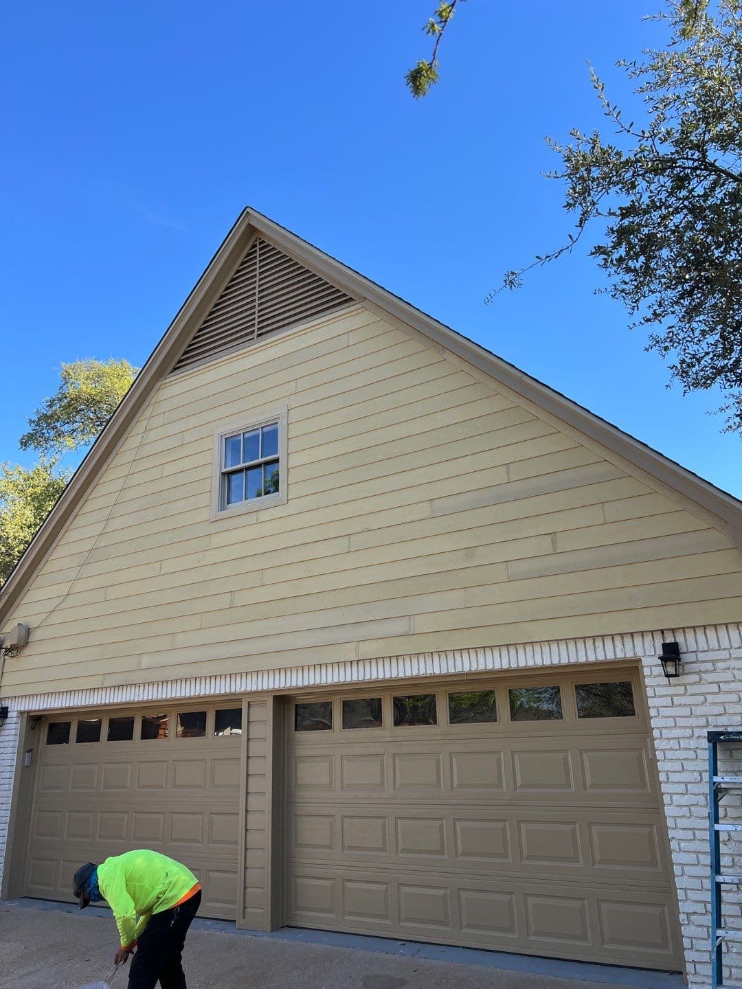 Tan two-car garage with horizontal siding, a small window, and a triangular attic vent.