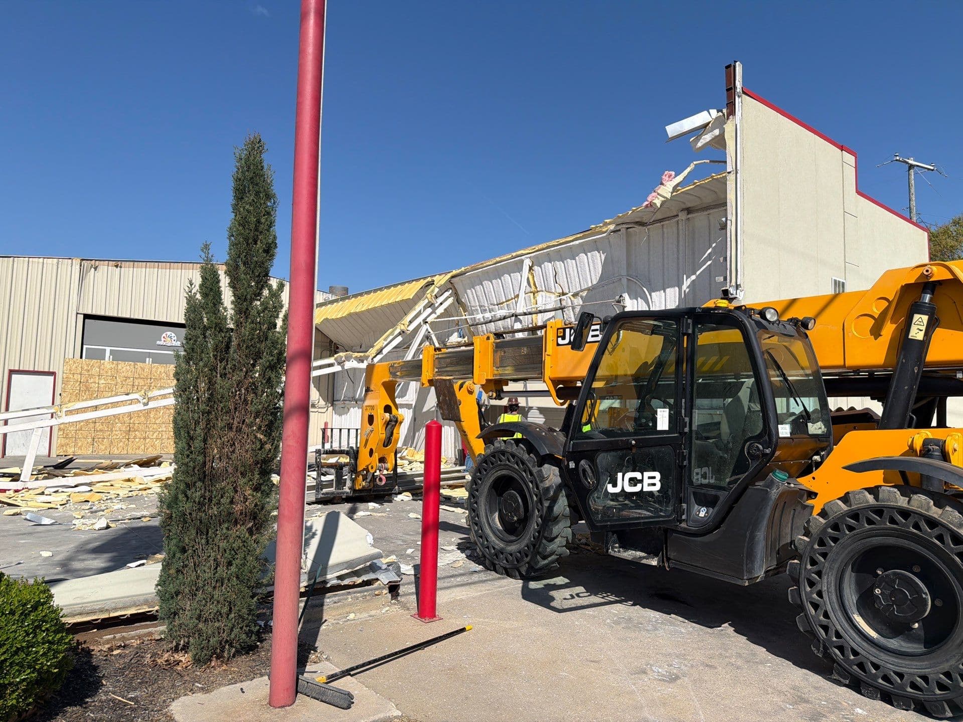 Yellow JCB telehandler parked in front of a partially demolished building with scattered debris.